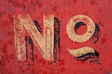 A faded sign with a red background and the word No in decaying yellow paint.