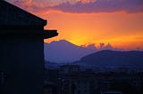 A sunset behind mount Vesuvius, looking over an Italian town with the silhouette of an apartment building in the foreground.