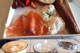 Smoked salmon, eggs, sausage and toast with two glasses of coffee and a glass of water in the foreground.