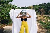 Woman in yellow pants with a disco ball in front of her face as though it’s her head.