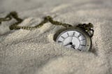 A Pocket Watch With Roman Numerals Lying In The Sand.