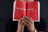 A Man Covering His Face With A Book With The Words, “Fail, Fail Again, Fail Better.” By Samuel Beckett