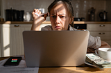 Tense woman reading content on a laptop in a kitchen.