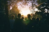 silhouette of group of people looking toward sunset through the trees