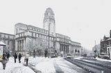 The Parkinson Building including the large clock tower, viewed from Woodhouse Lane. The paths and buildings are lightly covered in a recent snow shower. People are walking up the street.