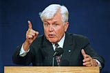 Grey-haired older man waving a finger.