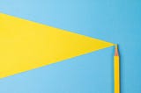 Photo of a yellow colored pencil on blue background with a yellow triangle shape drawn on it.