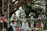 Bride and groom seated with family members and the priest at an Indian wedding