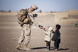 A soldier is giving a red fruit to two small children