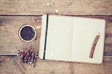 An open notebook with blank pages next to pine cones and a cup of coffee over a wooden table. Glitter overlies, inviting to annual reflection during Christmas time.