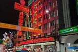 chinatown building with red neon lights and cars driving past in the foreground