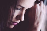 Woman resting forehead on hand against window, looking sad