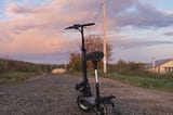An electric scooter is parked on a country road, as the sun sets.