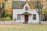 Repairing, upgrading, and staging a home for sale. Photo of a single family home with white picket fence. Autumn leaves are blanketing the front lawn.