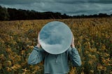 Person standing in a field holding a mirror