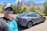 The author taking a selfie with the Tesla Model 3 in the background and beautiful Sedona mountains in the distance.