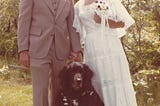 Outdoor wedding picture of groom, dog and bride.