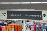 A sign demarcating aisles 27 and 28 in a Florida Walgreens reading, “27 Seasonal Incontinence 28”.