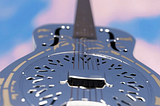 National Steel acoustic guitar flying into a cloud dappled clue sky, from Dire Straits’ “Brothers in Arms” LP cover