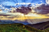 Stunning sunrise in blue and gold with sun peering behind grey cloud