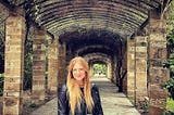 A young blonde in glasses woman standing in the center of a brick archway in Europe