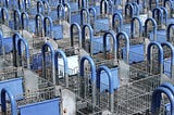 Hundreds of shopping carts lined up organized, blue plastic covering gray metal. A consumer’s heaven.