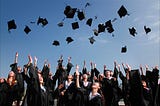 Newly graduated people wearing black academy gowns throwing hats up in the air