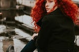 Red haired woman sitting on the ground.