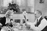 A man and woman sitting at a table reading a newspaper