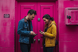 A man and a woman standing across from each other while holding their phones.
