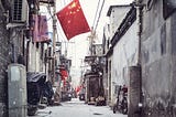 A Chinese flag overhanding and urban street with snow falling.