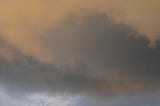 Photo of storm clouds yellow on dark with a bare tree top beneath