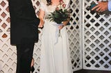 The image is an author provided picture of her wedding as an 18 year old woman to a 30 year old man. Her expression is unreadable, but not the happy expression you’d expect of a bride. His head is out of the frame. She is holding a bouquet of roses and the officators hands and bible are visible to the right side of the frame. A closer look reveals the bride’s child hiding behind the groom’s legs.