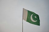 A picture of Pakistan Flag with a grey cloudy sky backdrop.