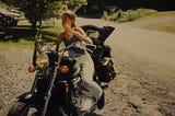 Photo of a thin young woman sitting on a large motorcycle.