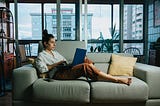 Woman working on laptop while lounging on couch at home
