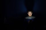 Main sits in darkness, light of phone illuminates his face.