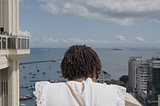 Uma mulher negra, de cabelos curtos e cacheados, observa a cidade próxima ao Elevador Lacerda, ponto turístico de Salvador, na Bahia.