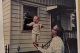 Me at six months, balanced in Grandaddy’s hand and standing upright outside of their house in the yard.