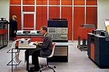 Two people are operating large computers and mainframes. Image from the IBM archives.