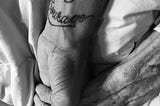 A young hand with “Strength and Courage”   tattooed on the inner wrist holds an older hand.