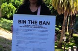 Image of Awatea at the launch of the Open Letter holding a sign that reads ‘Bin the Ban’ with Myers Park and the city in the background.