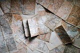 An overhead shot of many maps lying flat on an unseen surface