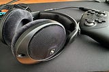 A pair of Sennheiser HD560S headphones lying on their side on a desk mat near a Switch 2 Pro controller.