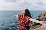 person standing by ocean joyously spreading arms
