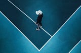 A man immersed in virtual reality is wearing a VR headset and walking on a blue tennis court. He seems to be lost in another universe