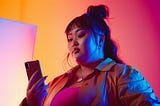 Unsmiling Asian woman looks at her phone with a colorful background