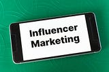 A phone sits on a green background with words written “influencer marketing”.