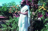 Osho, dressed in white, stands peacefully amidst the green grass.