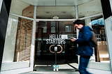 Man walking past glass double door that reads: Hello Startups